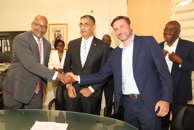 UTS shareholder representative, Mister of Justice, Cornelius De Weever shaking hands with Nicholas Collette at conclusion of signing. In center is Finance Minister Perry Geerlings and looking on are UTS CEO Paul de Geus and Finance Ministry staffers.